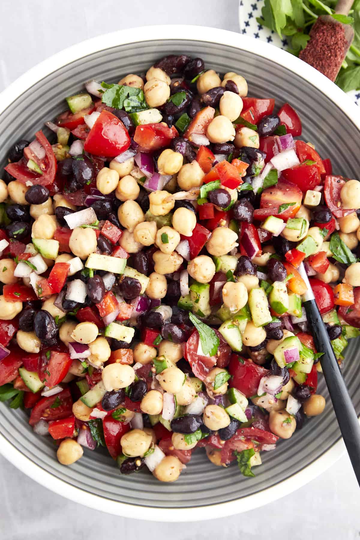A bowl of balela salad with chickpeas, black beans, fresh veggies, and herbs. 