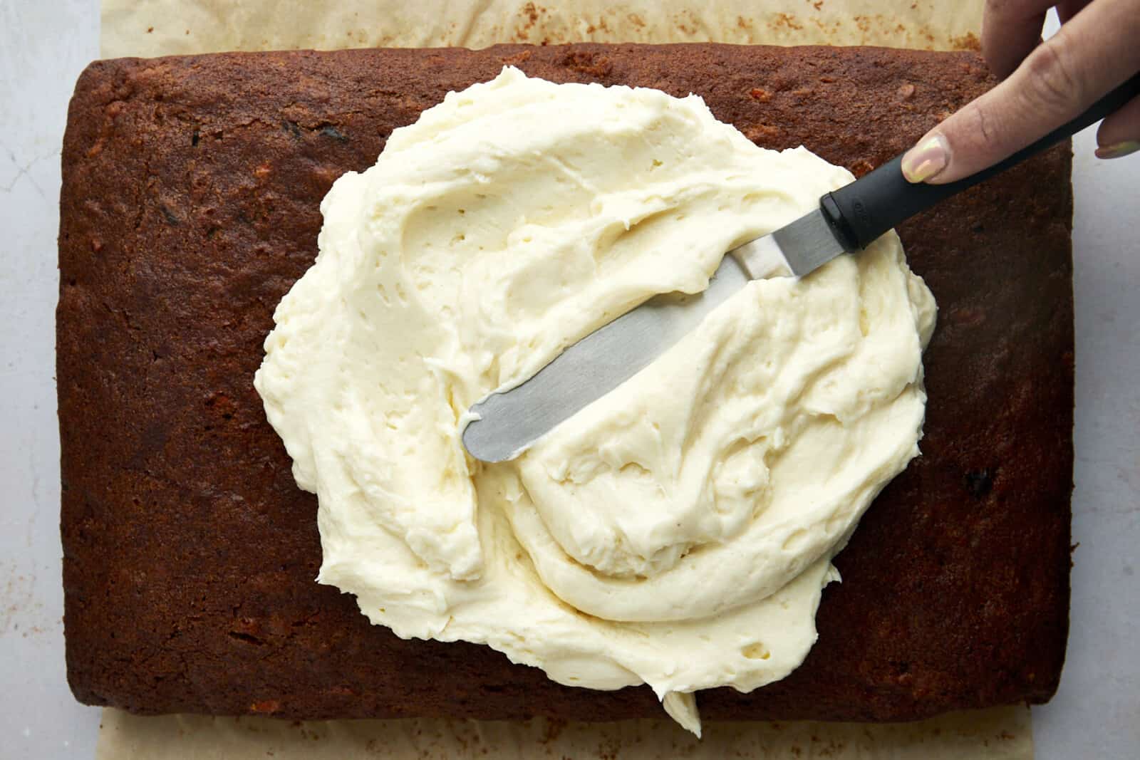 Cream cheese frosting being spread over carrot cake. 