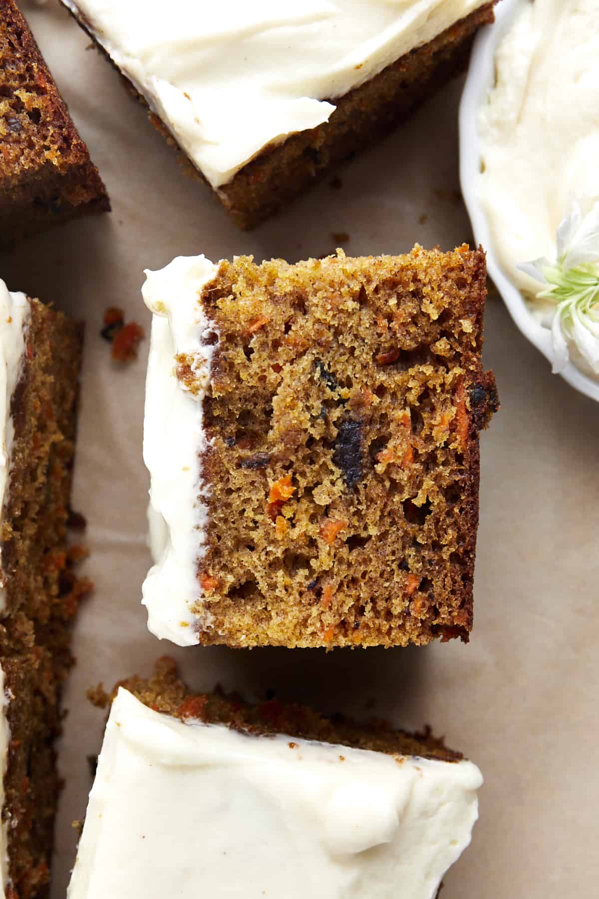 Side view of a piece of carrot cake topped with cream cheese frosting showing the shredded carrots and nuts in the batter. 