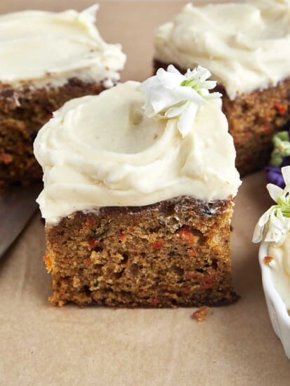 A square piece of carrot cake topped with cream cheese frosting.