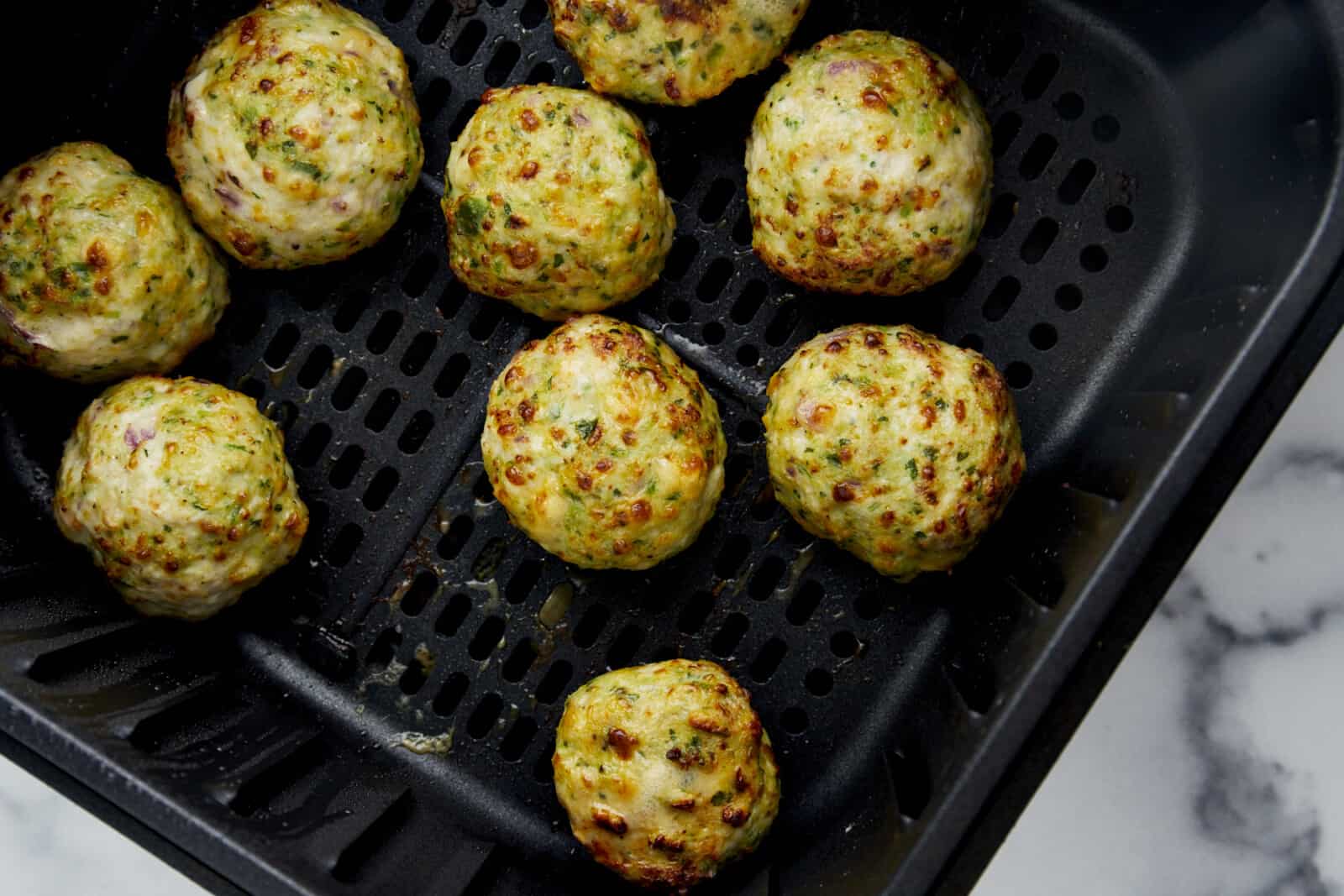 Cooked Air Fryer Jalapeño Cheddar Chicken Meatballs in an air fryer basket.
