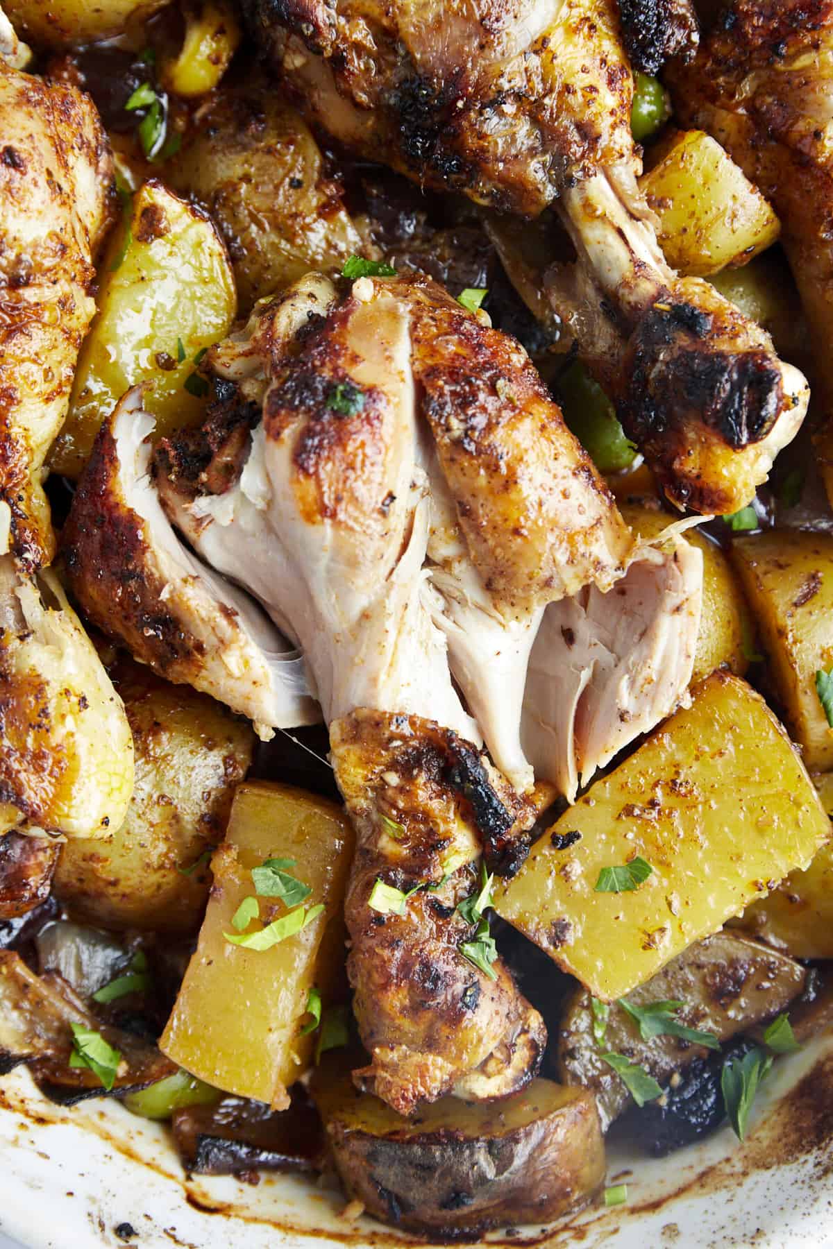 Oven baked chicken drumsticks with potatoes exposing the meat.  