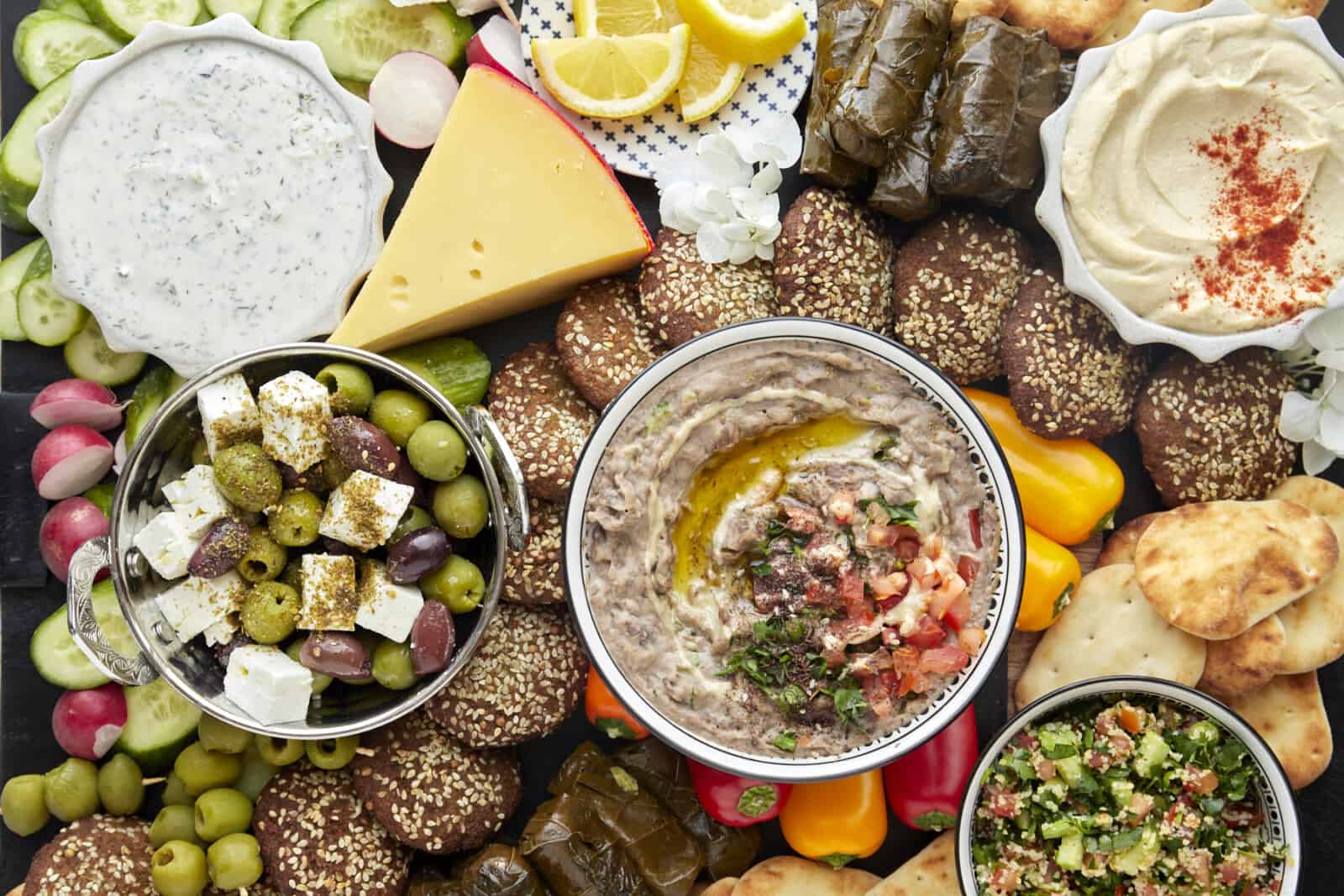 Close up image of a mezze platter with toum, tzatziki, baba ganoush, tabbouleh, and olives.