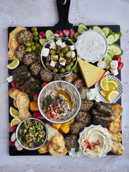 Overhead image of a large Mediterranean mezze platter with dips, veggies, bread, cheese, stuffed grape leaves, and olives.