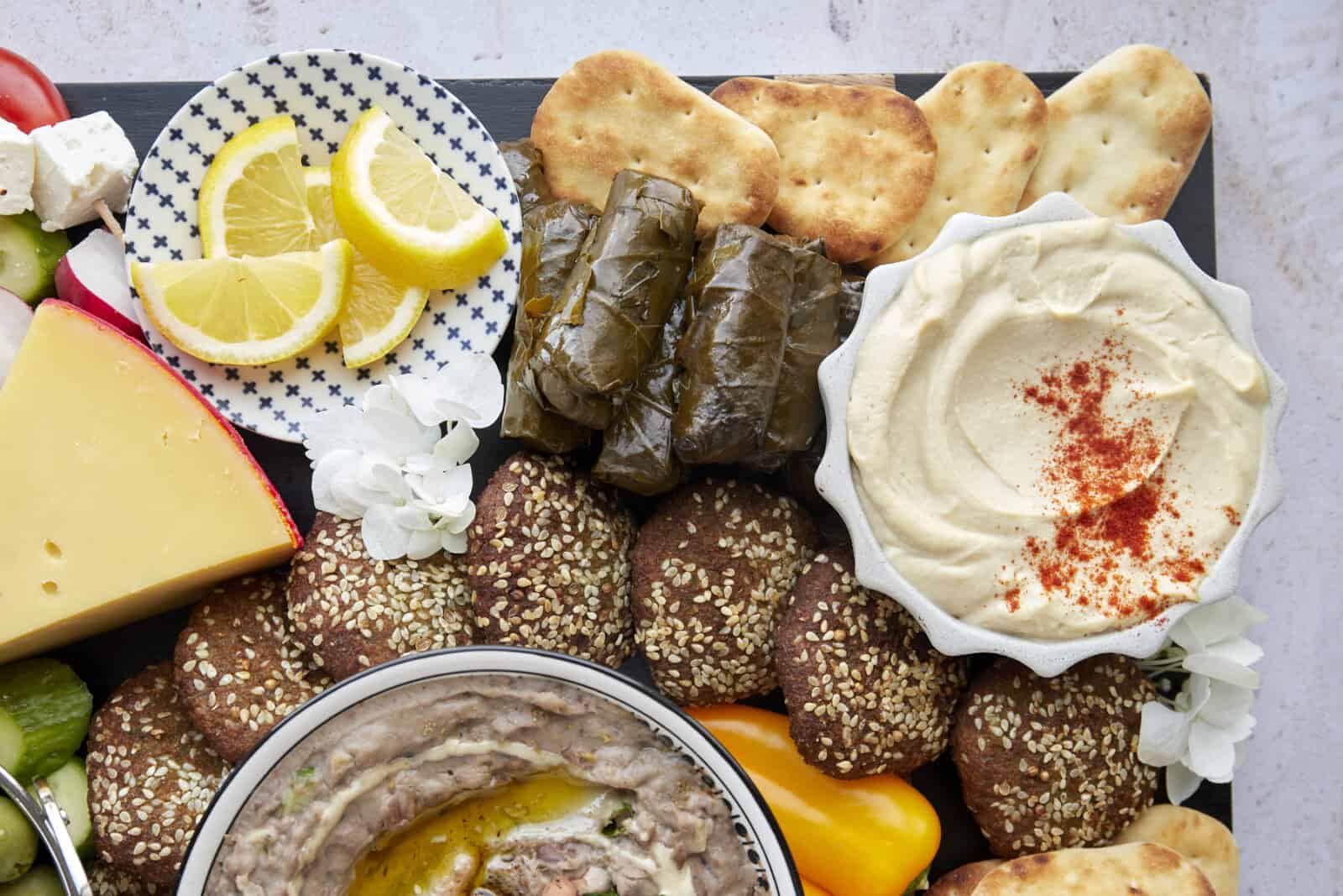 Close up of a section of a mezze platter featuring toum, pita, stuffed grape leaves, falafel, and lemon wedges. 