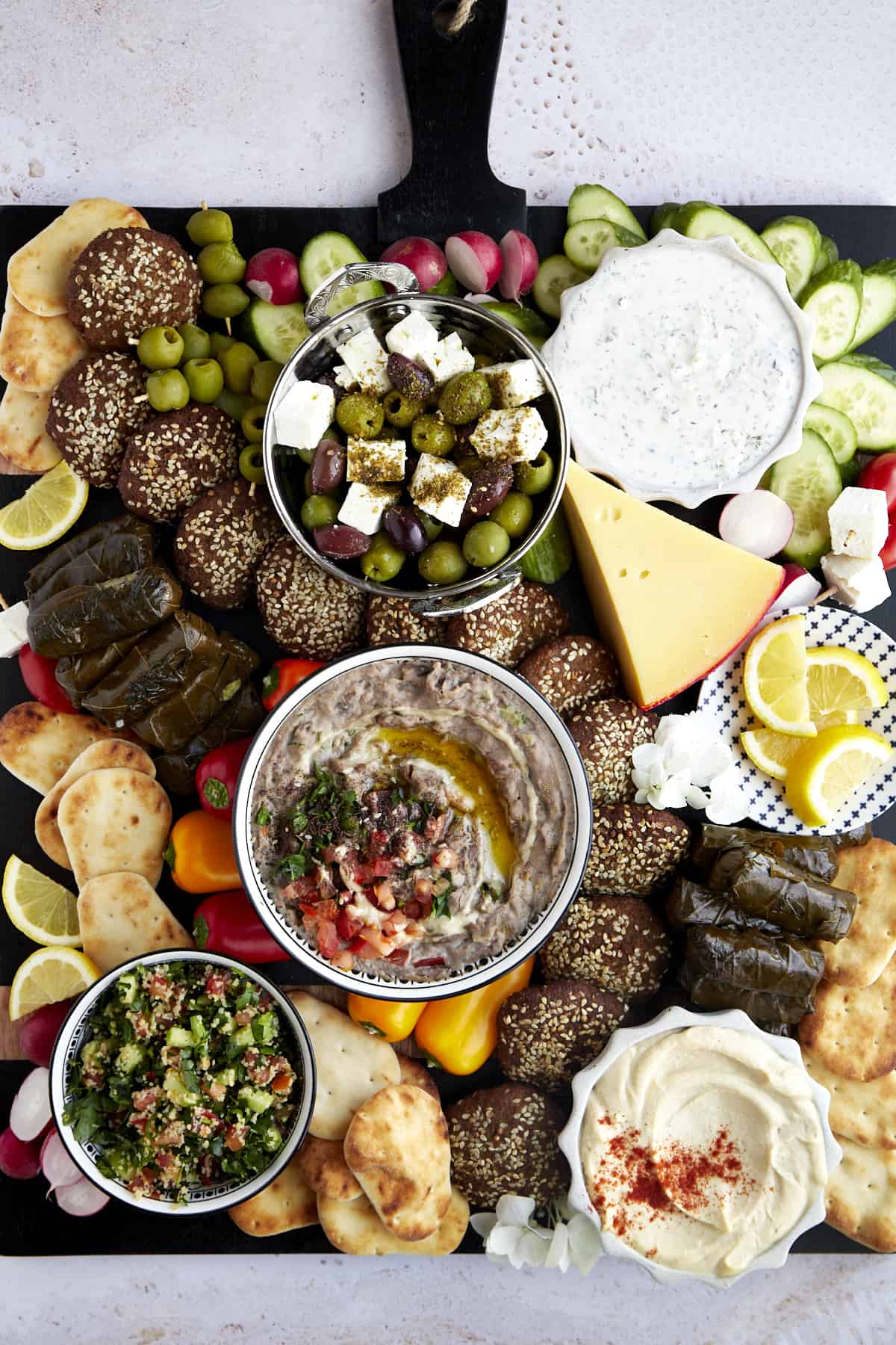Overhead image of a mezze platter with dips and spreads, cheese, fresh veggies, pita, falafel, and stuffed grape leaves. 