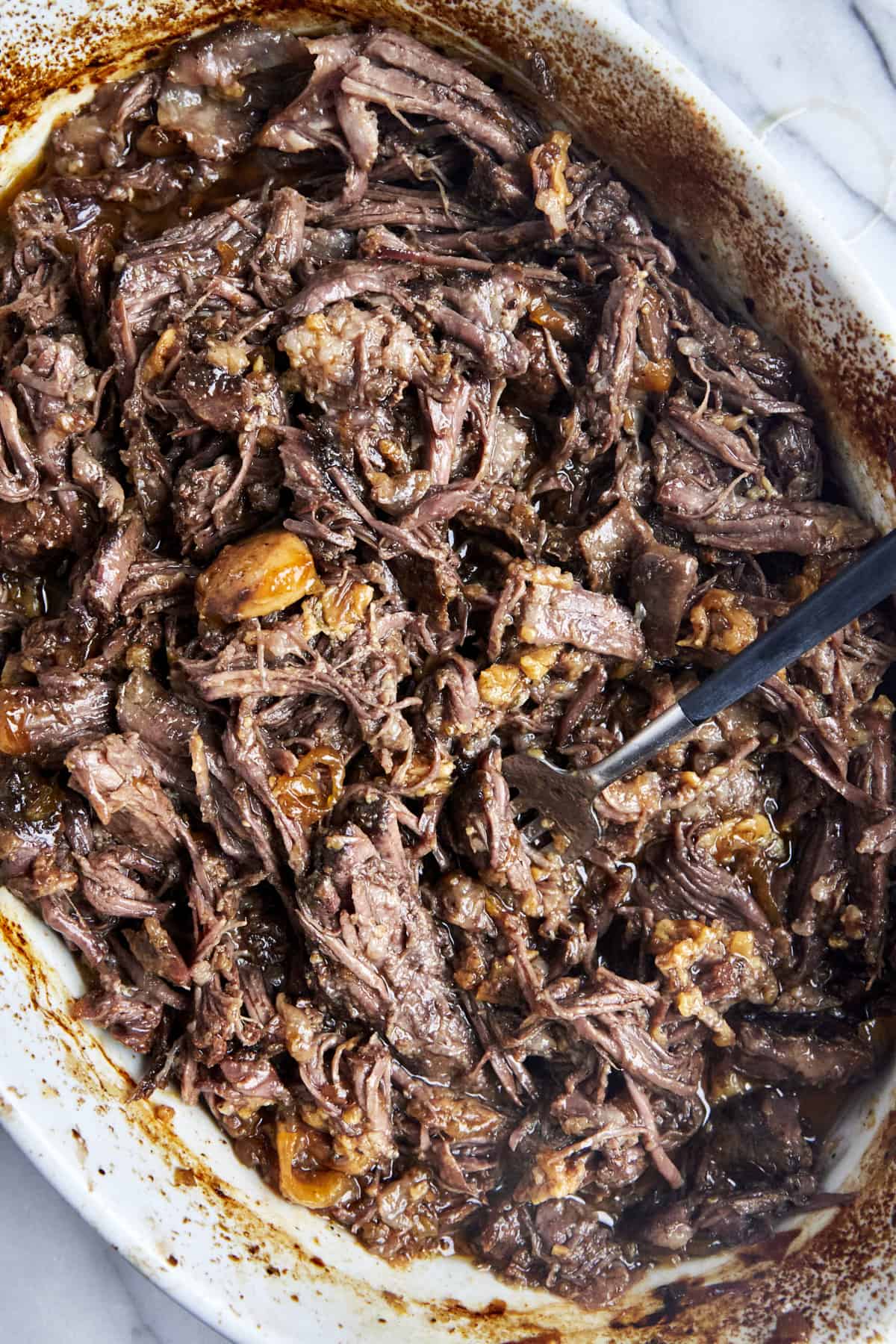 Shredded beef chuck roast in a baking dish with onions and garlic. 