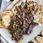 Hummus with meat on a platter with pita chips on the side.