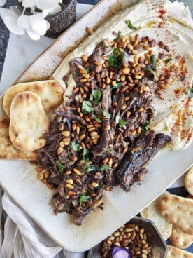 Hummus with meat on a platter with pita chips on the side.