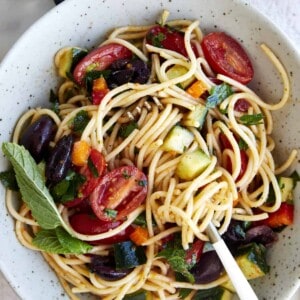 A bowl of Greek spaghetti pasta salad with noodles twined around a fork.