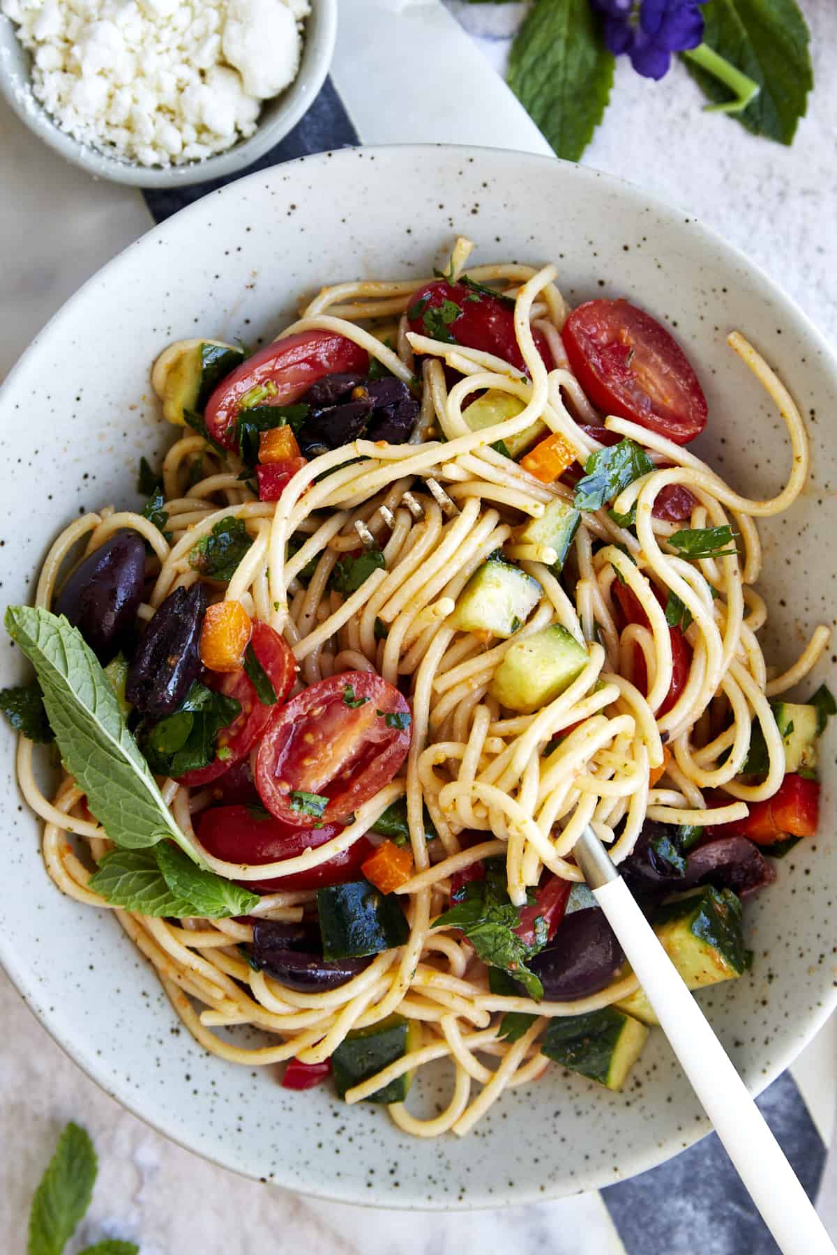 A bowl of spaghetti pasta salad with fresh veggie and a sun-dried tomato dressing with a fork sticking out. 