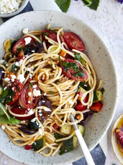 A bowl of Greek spaghetti pasta salad topped with feta with noodle twirled around a fork.