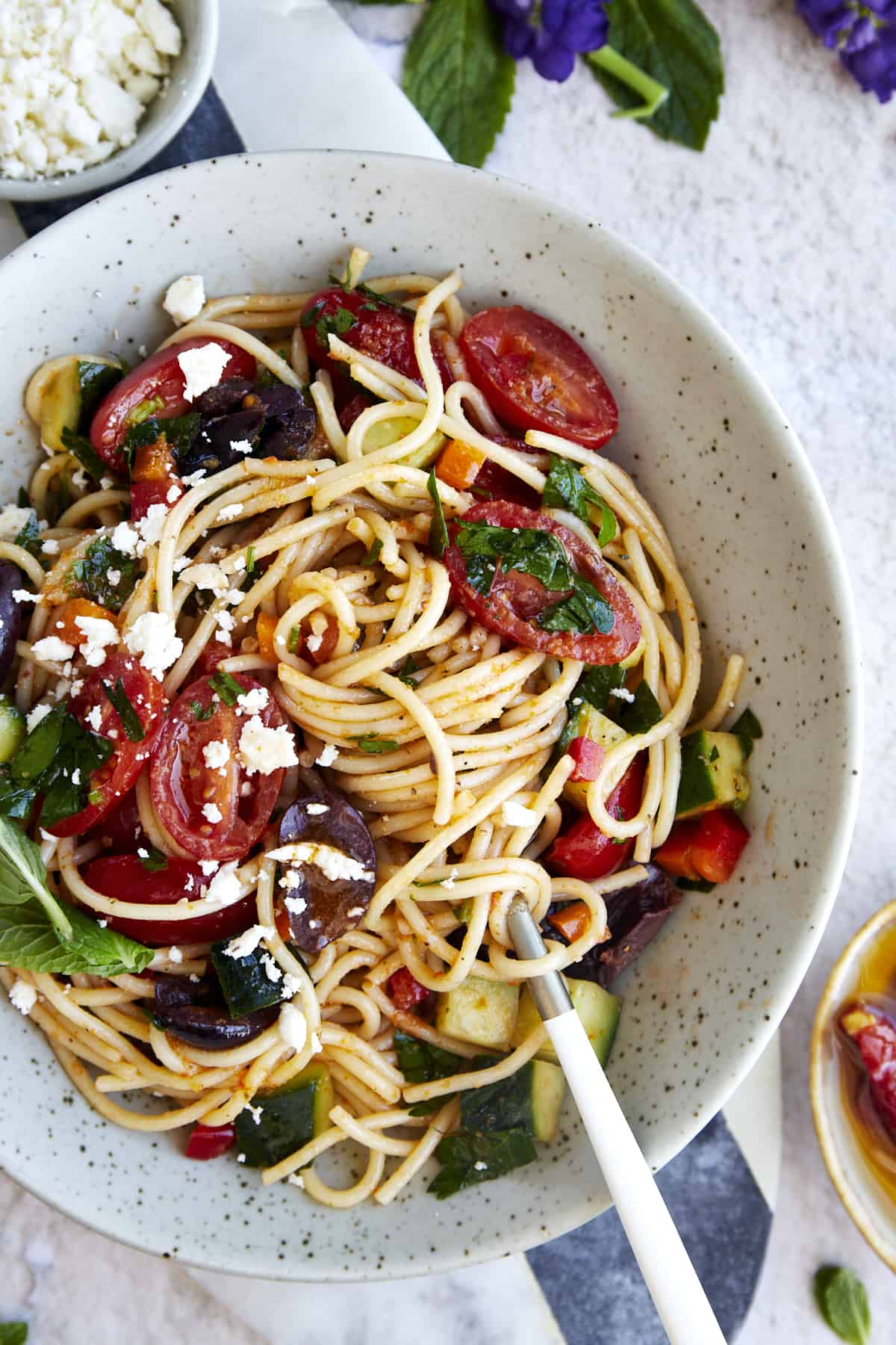 A bowl of Greek spaghetti pasta salad topped with feta with noodles twirled around a fork. 