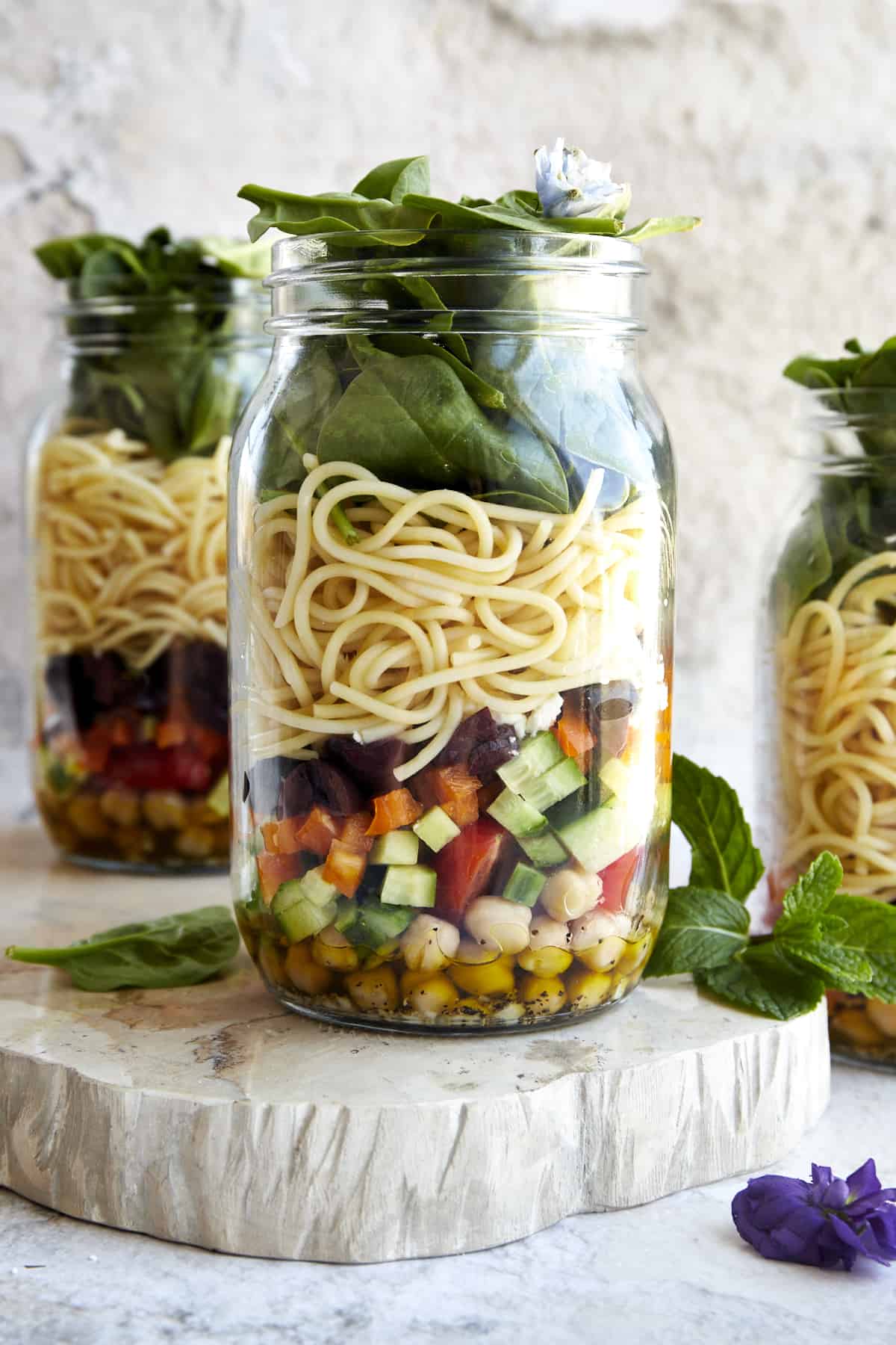 A mason jar salad with an olive oil dressing in the bottom, chickpeas, chopped veggies, spaghetti, and spinach. 
