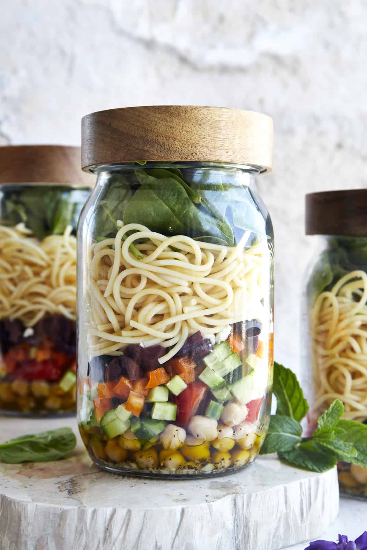 A mason jar salad with olive oil dressing, chopped veggies, spaghetti, and spinach with the lid on top. 