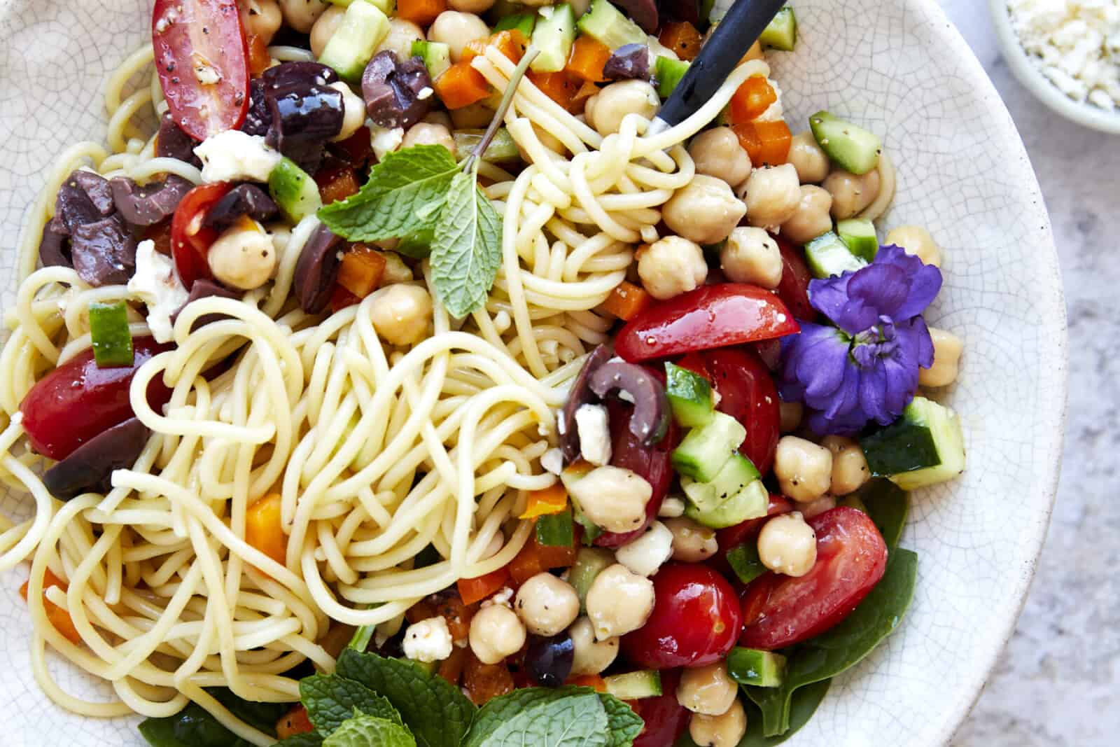 A bowl of spaghetti salad with a fork twirled around the noodles. 