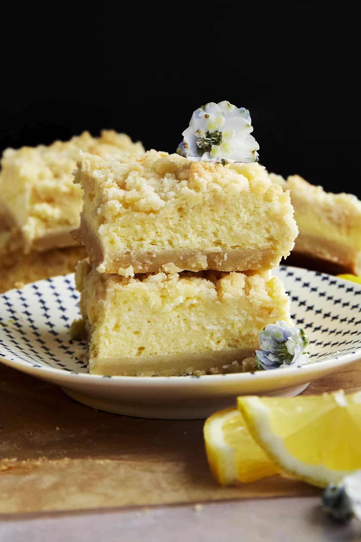 Two lemon cheesecake bars stacked on top of each other on a plate. 