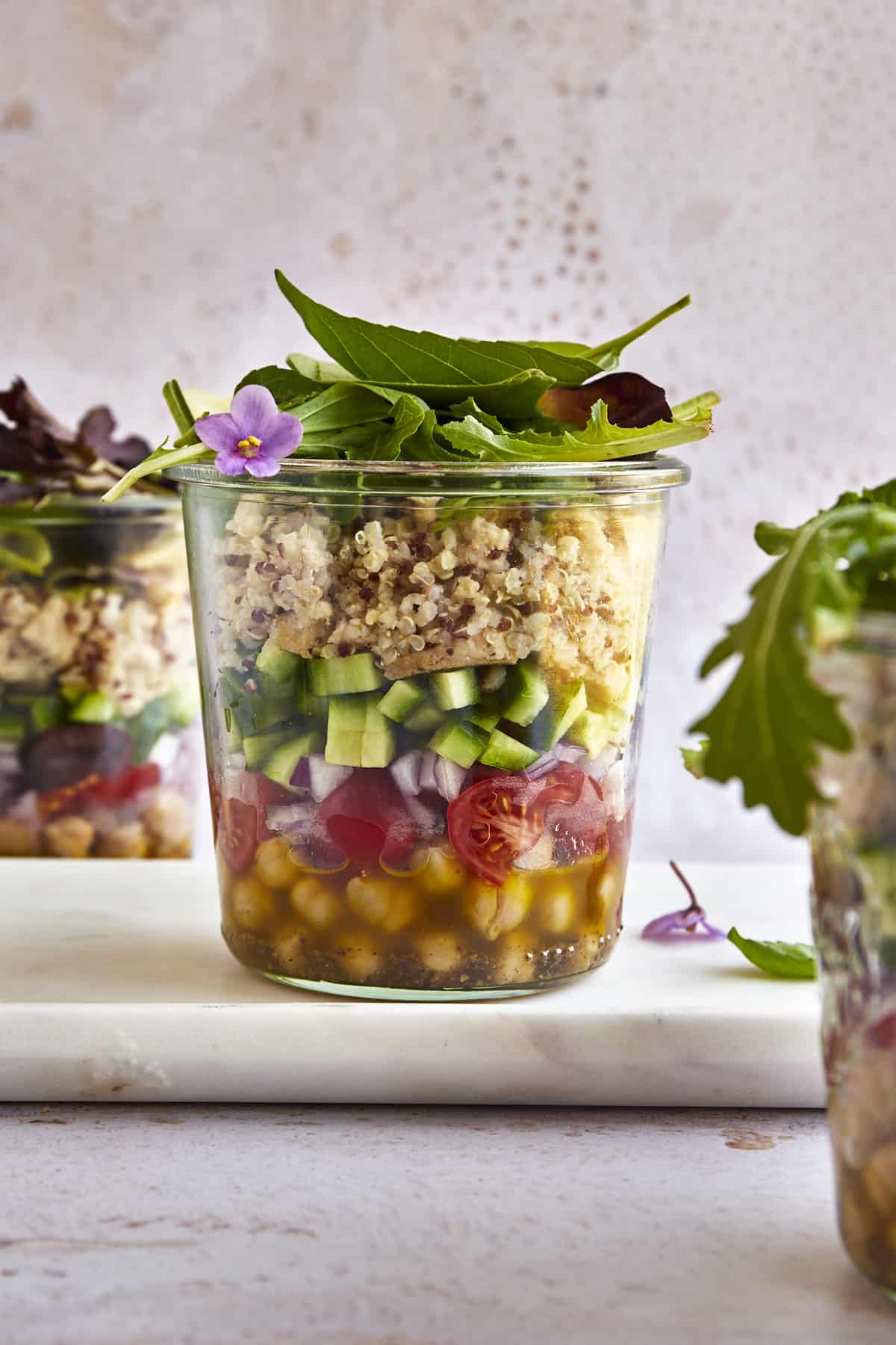 A salad in a jar with olive oil dressing, chickpeas, tomatoes, red onion, cucumbers, chicken, quinoa, and greens. 