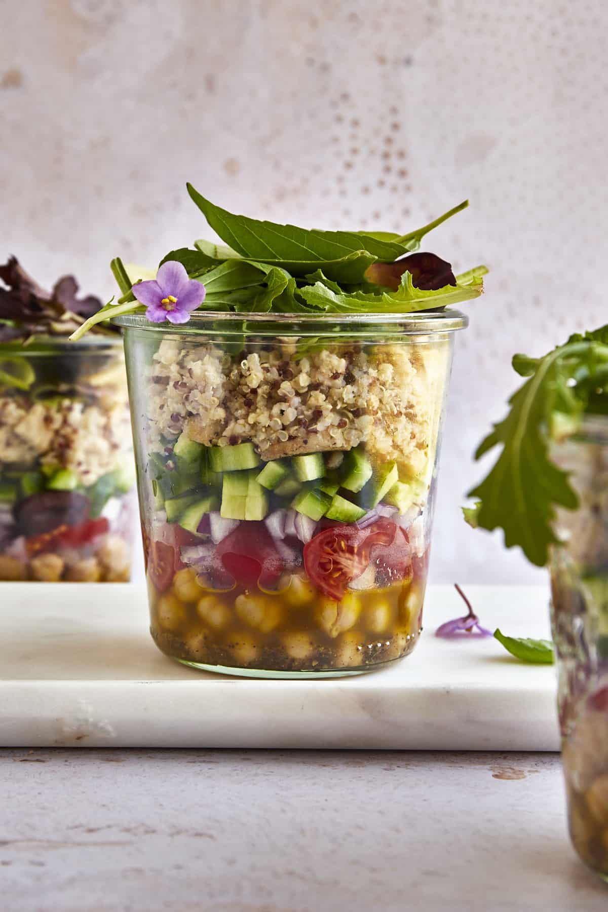 A salad in a jar with olive oil dressing, chickpeas, tomatoes, red onion, cucumbers, chicken, quinoa, and greens.