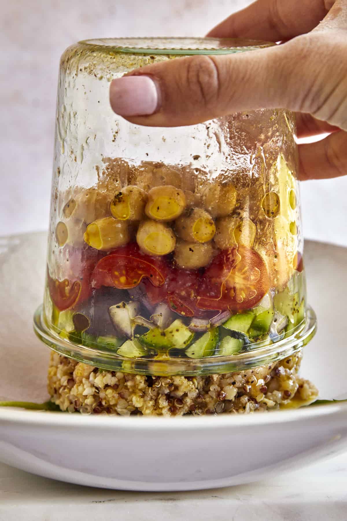 A Mediterranean quinoa salad in a jar being inverted into a bowl. 
