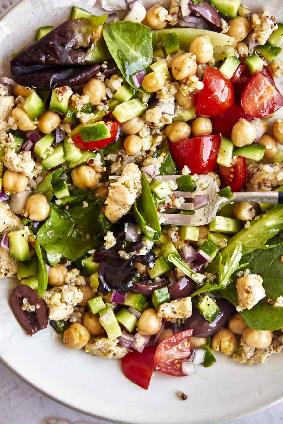 Overhead image of a salad in a jar containing greens, veggies, quinoa, chicken, and chickpeas that has been dumped into a bowl. 