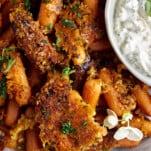 Close up image of Parmesan oven roasted carrots with a bowl of tzatziki on the side.
