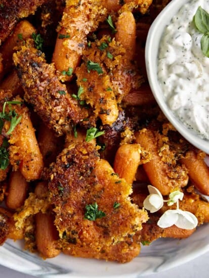 Close up image of Parmesan oven roasted carrots with a bowl of tzatziki on the side.