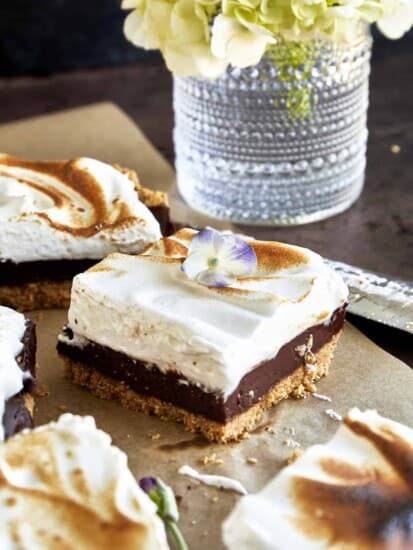 Side view of a s'mores bar with layers of graham cracker crust, chocolate ganache, and a meringue topping.