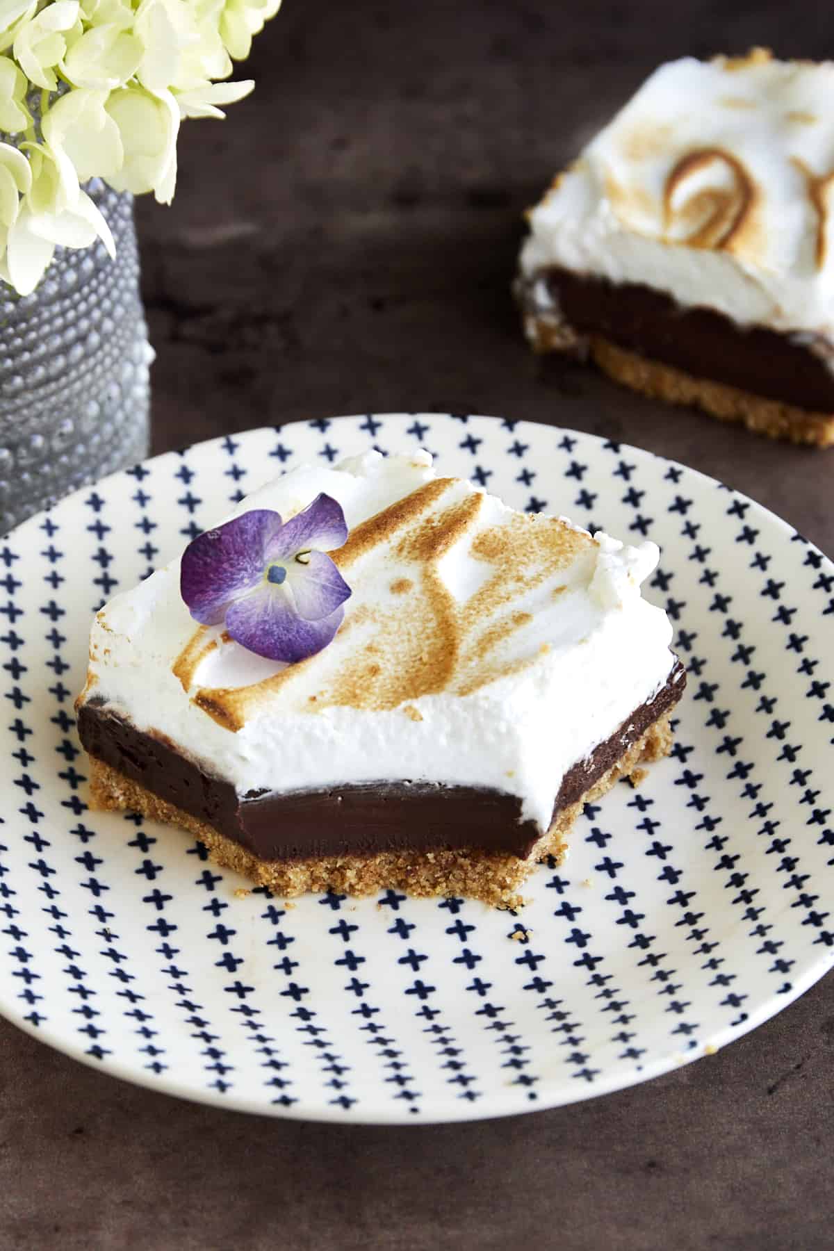 A sliced s'mores bar with a graham cracker layer, a chocolate ganache layer, and a meringue layer on top with a bite missing. 