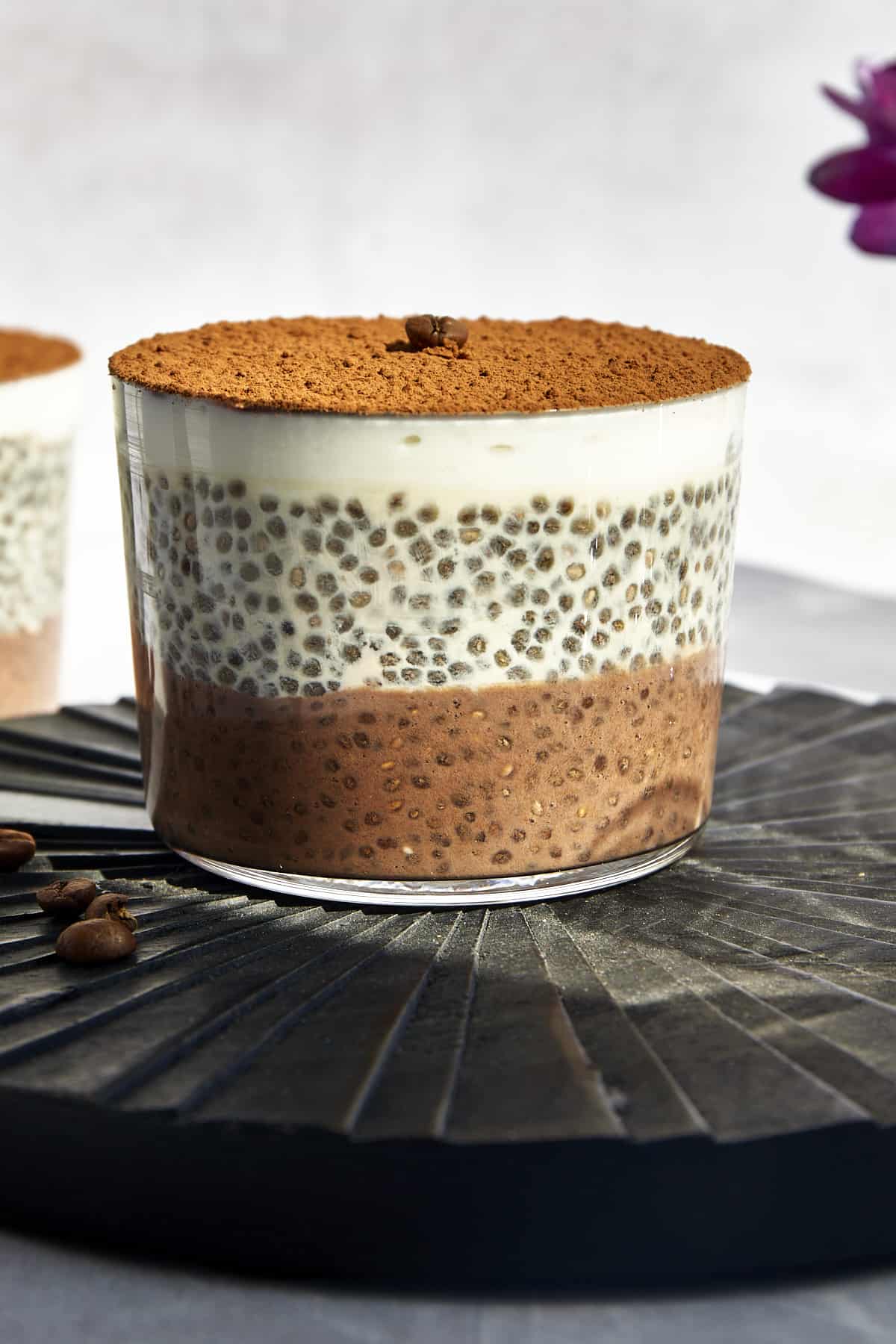 A jar of layered tiramisu chia pudding with a coffee layer, vanilla layer, yogurt layer, and cocoa powder on top.