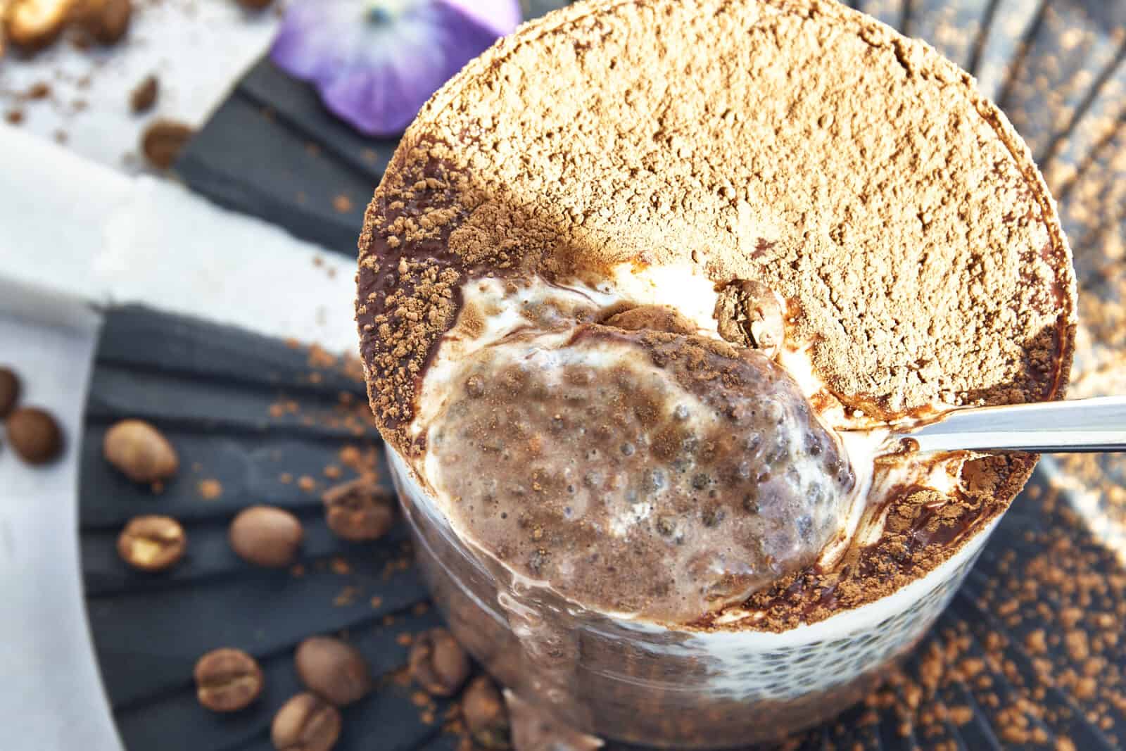 A spoon lifting a bite of tiramisu chia seed pudding from a jar. 