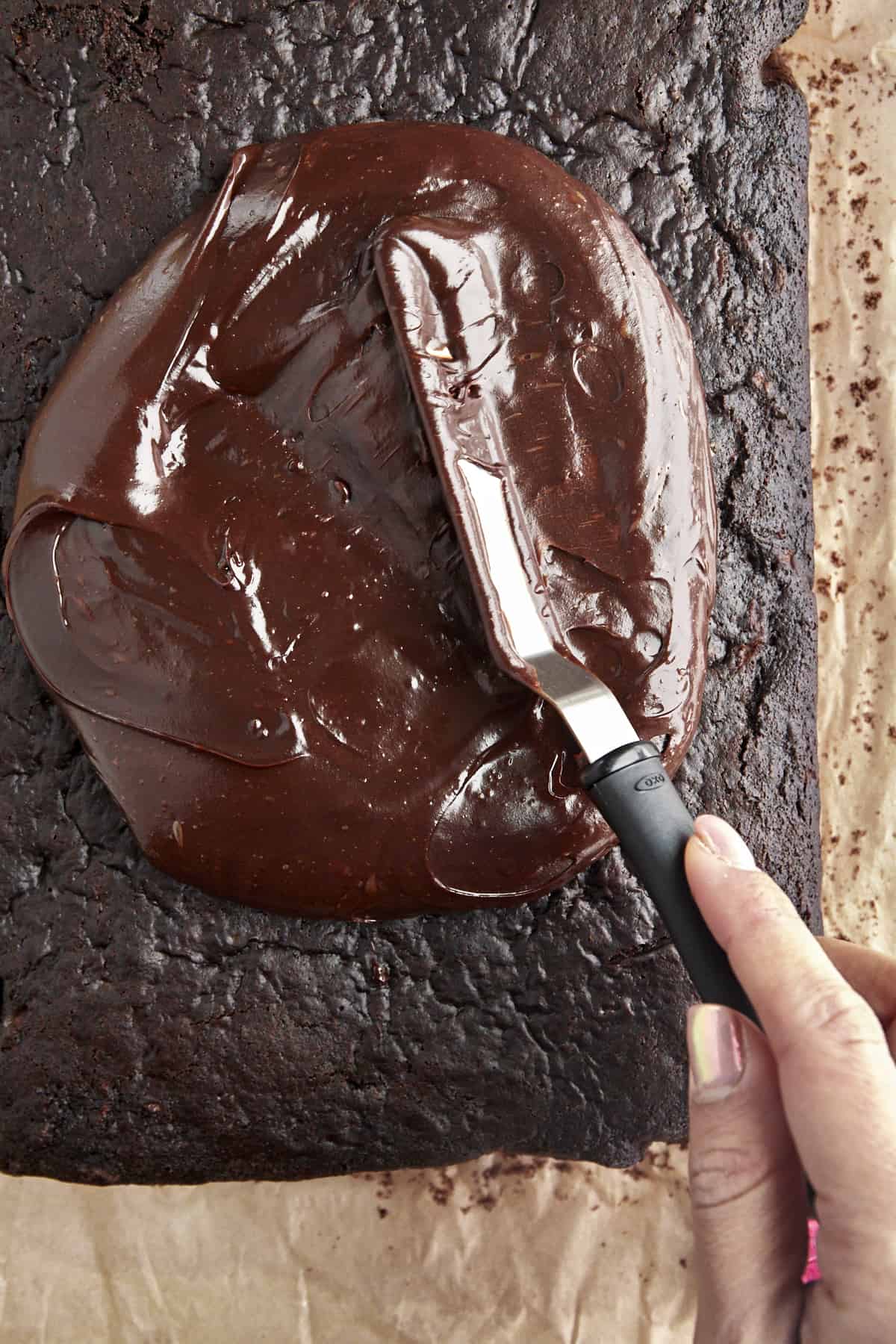 Chocolate frosting being spread evenly over the zucchini cake. 
