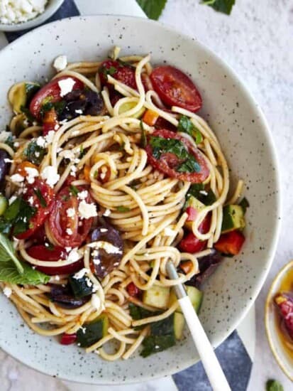 A bowl of Greek spaghetti pasta salad topped with feta with noodle twirled around a fork.