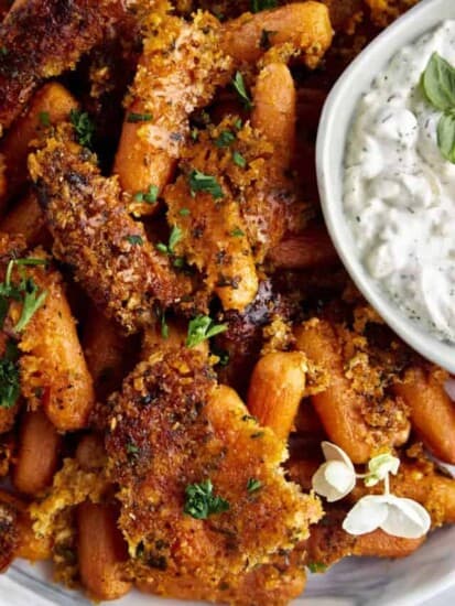 Close up image of Parmesan oven roasted carrots with a bowl of tzatziki on the side.