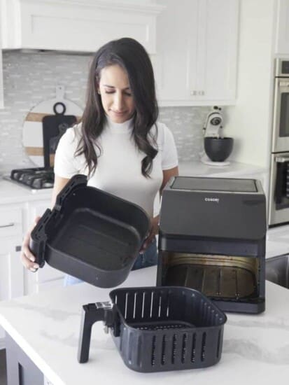 A woman disassembling a dirty air fryer.