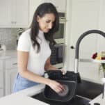 A woman using a sponge to clean the basket of an air fryer in a sink.