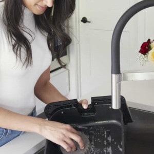 A woman using soap and water to clean an air fryer basket in a sink.