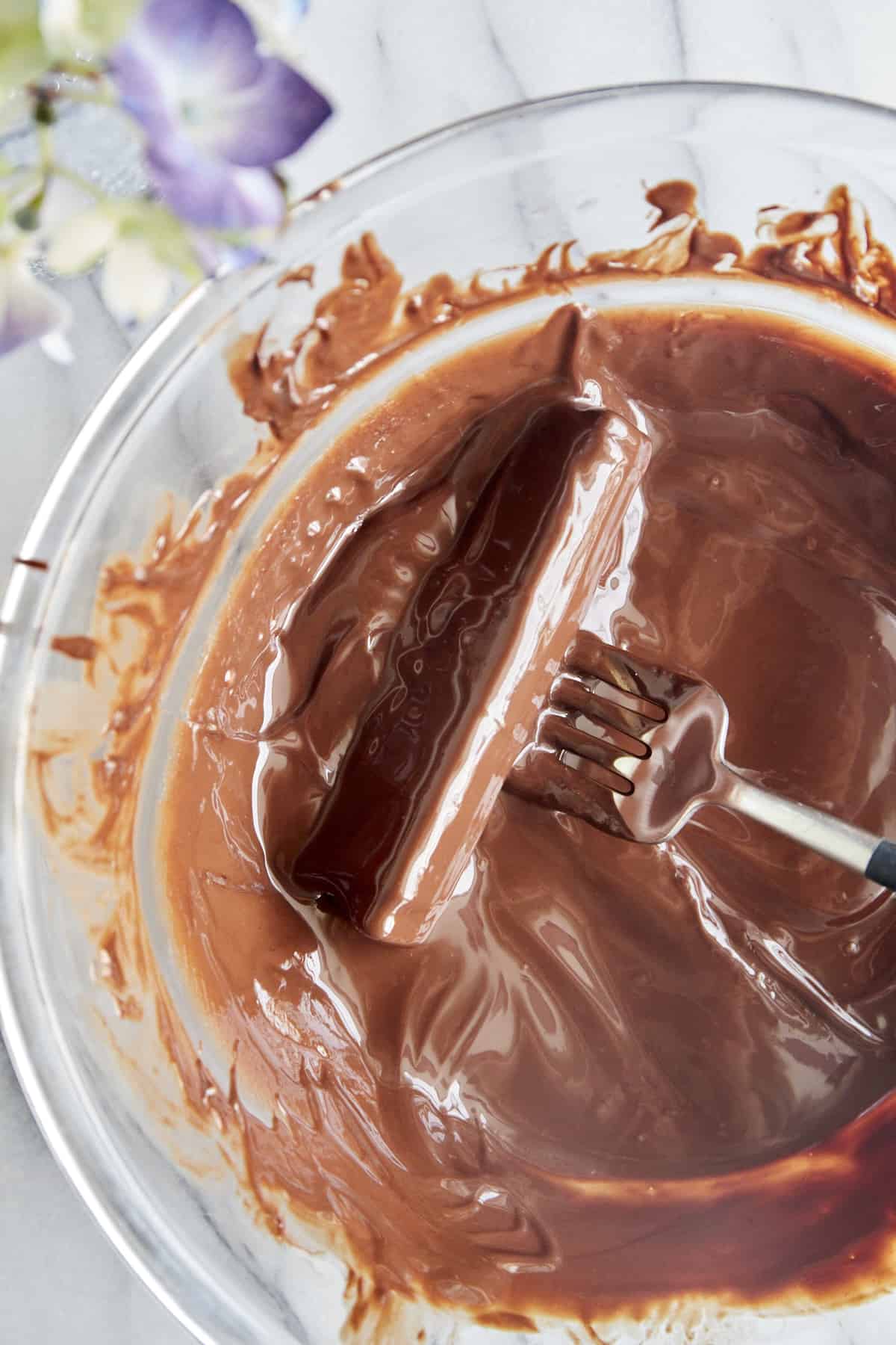Overhead image of a fork rolling a peanut butter stuffed celery stick in a bowl of melted chocolate. 