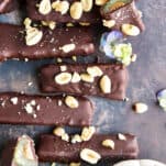 Overhead image of chocolate dipped celery and peanut butter logs topped with peanuts and sea salt with one log sliced in half.