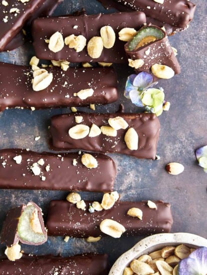 Overhead image of chocolate dipped celery and peanut butter logs topped with peanuts and sea salt with one log sliced in half.