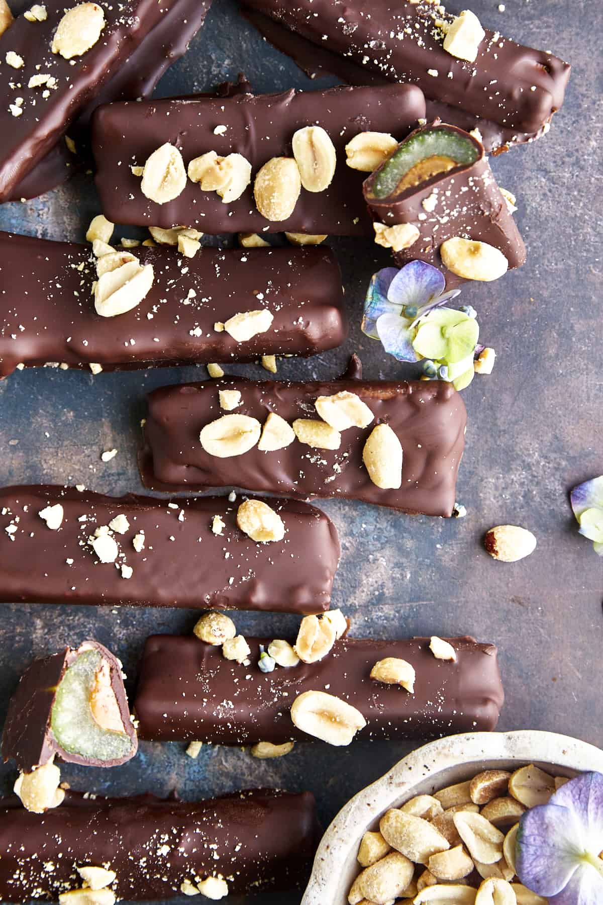 Chocolate covered celery and peanut butter sticks topped with peanuts and sea salt with a bite missing from one. 
