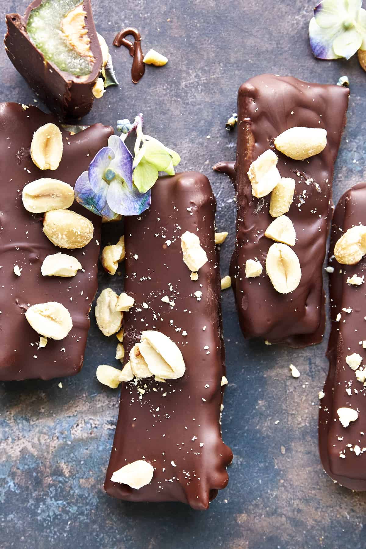 Four full-sized chocolate celery and peanut butter logs topped with peanuts and sea salt and a fifth log with a bite missing.