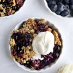 Overhead image of a ramekin full of blueberry crisp topped with vanilla ice cream.