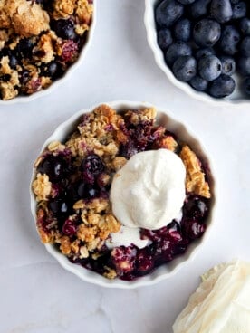 Overhead image of a ramekin full of blueberry crisp topped with vanilla ice cream.