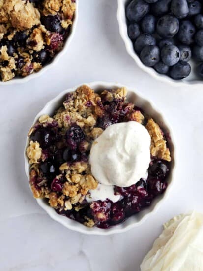 Overhead image of a ramekin full of blueberry crisp topped with vanilla ice cream.