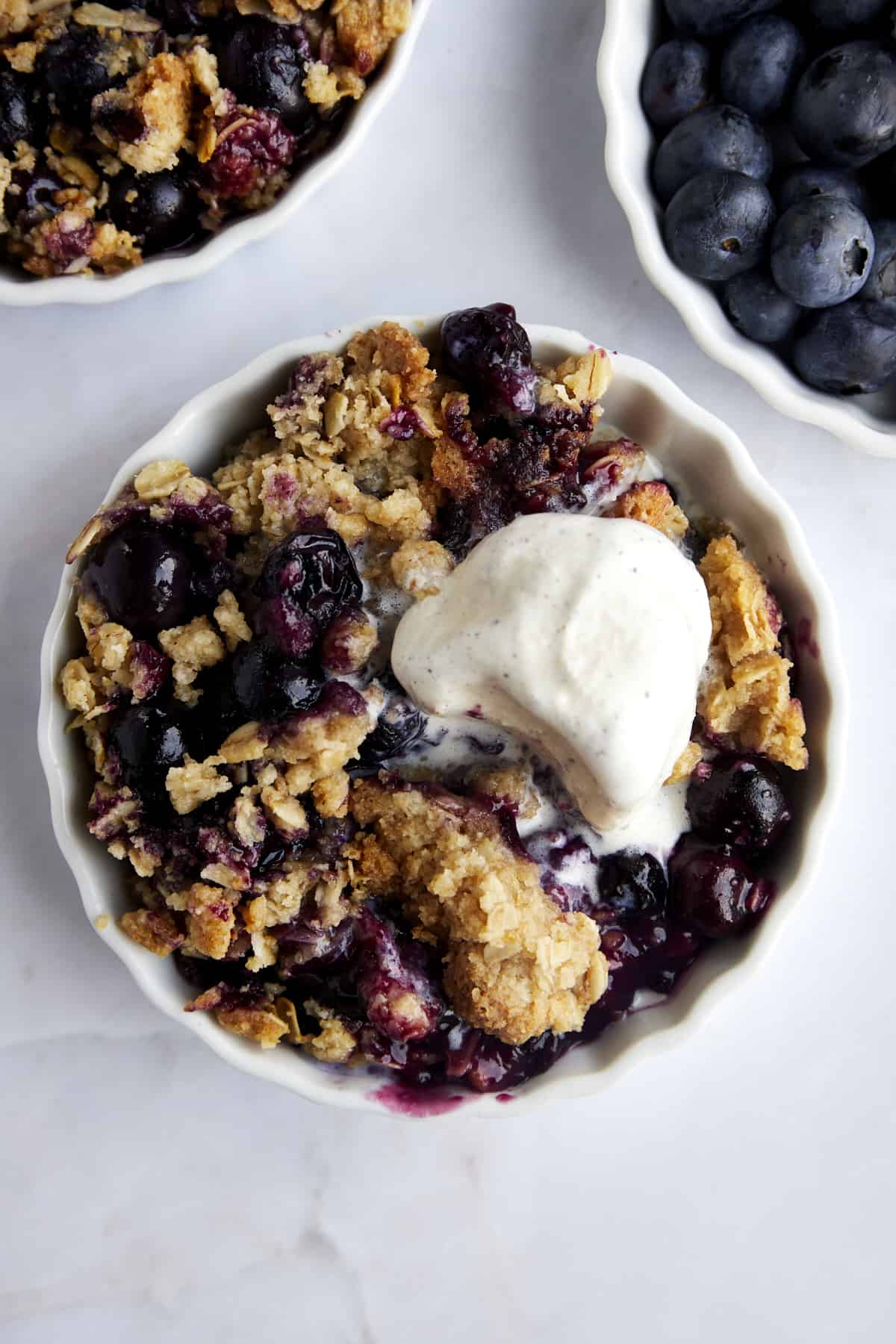 A small ramekin with a serving of blueberry crisp topped with vanilla ice cream. 