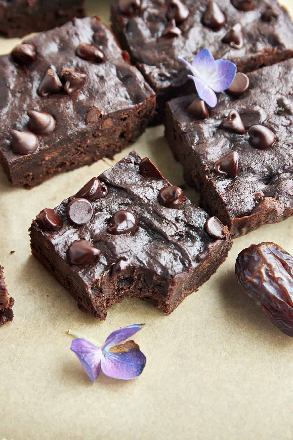 A fudgy date brownie topped with chocolate chips with a bite missing from the corner. 