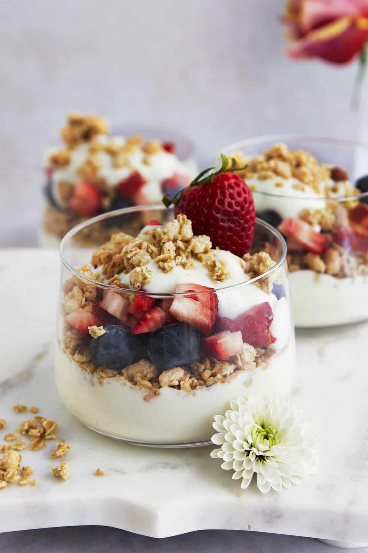Side view of a yogurt parfait with granola, blueberries, strawberries, and honey. 