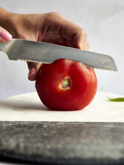 A side view of the top of a tomato being sliced off.