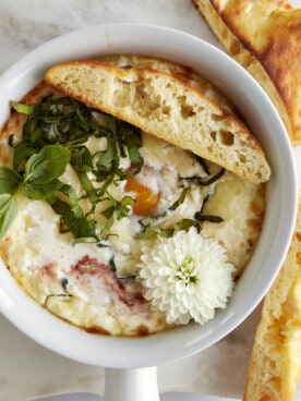 Overhead image of a ramekin with Eggs in Purgatory and a piece of bread on top.